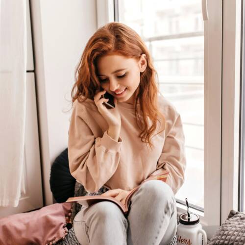 Woman on a phone call by a bright window at home