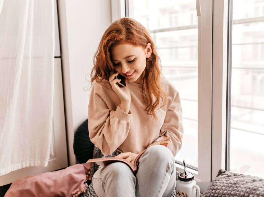 Woman on a phone call by a bright window at home