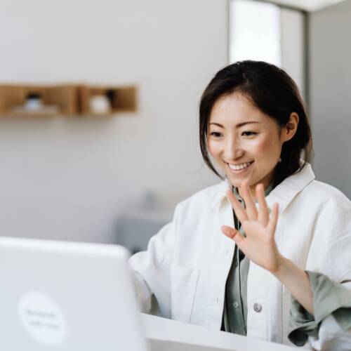 Smiling woman greeting her therapist on a video call in a bright, minimal room