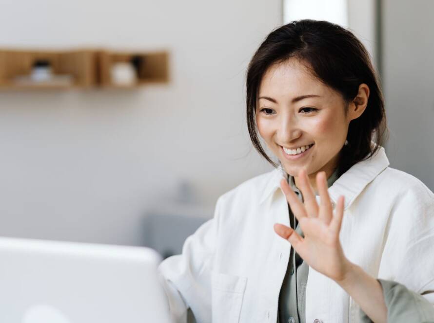 Smiling woman greeting her therapist on a video call in a bright, minimal room