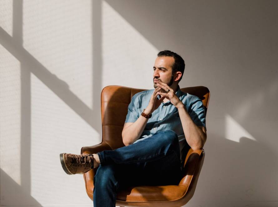 Man sitting thoughtfully in a leather armchair in a bright, minimal room with soft window light